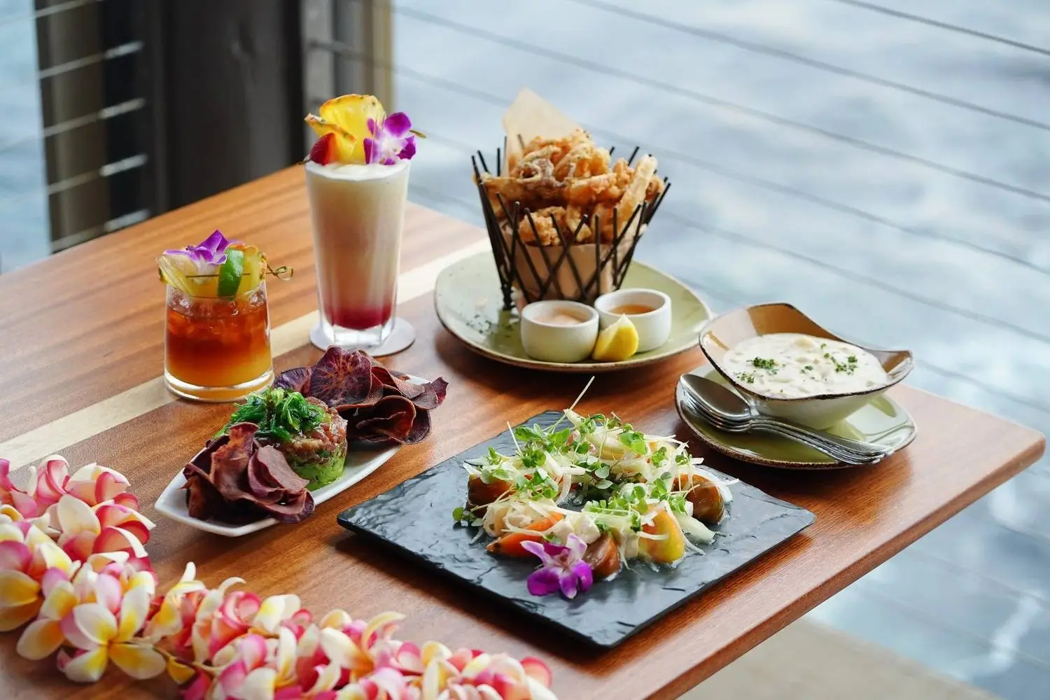 A table set with cocktails and shared plates above the water